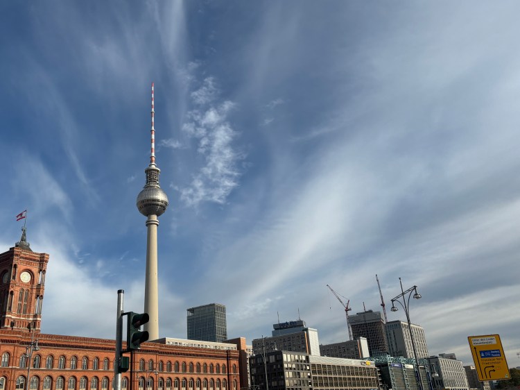 Blick auf den Berliner Fernsehturm und das Rote Rathaus, umgeben von modernen Gebäuden und blauem Himmel.