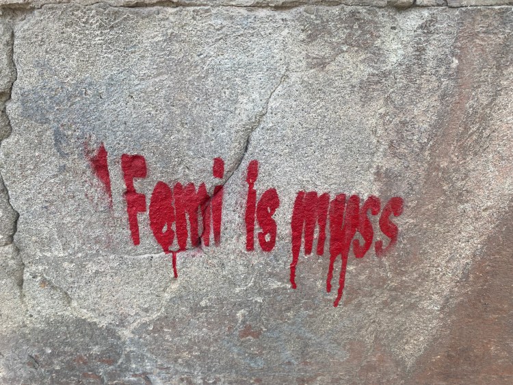 Graffiti mit der Aufschrift 'Femi is myss' in roter Farbe auf einer grauen Steinwand.